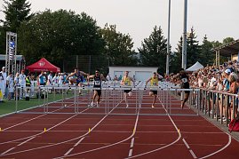 Mehrere Athleten im Hürdenlauf springen gleichzeitig über die Hürden. Zuschauer verfolgen den Lauf von der Tribüne und am Bahnrand.