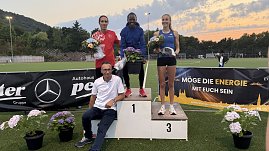 Drei Athlet:innen stehen auf dem Siegerpodest mit Blumen in den Händen, vor ihnen Mercedes-Benz Pkw Verkaufsleiter Jörn Bierwisch mit weißem Shirt. Hinter dem Podest Sponsorenbanner und Abendhimmel.