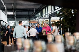Mehrere Menschen stehen und unterhalten sich in der Eingangshalle des Autohauses. Im Hintergrund sind Glasfassaden und Pflanzen sichtbar.