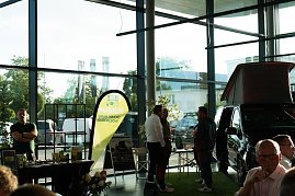 Ein Messestand mit gelb-gr&uuml;nem Banner M&ouml;bius � Gr&uuml;n macht gl&uuml;cklich!. Daneben ein schwarzer Mercedes-Camper mit hochgeklapptem Dach. Zwei M&auml;nner und weitere Personen unterhalten sich.