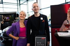 Eine Frau (Moderatorin Mandy Kossira) in lila Blazer und pinkem Top steht neben einem Mann im schwarzen Anzug. Beide l&auml;cheln. Neben ihnen ein Aufsteller mit der Aufschrift Mein Fischer.