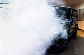 Eine schwarze Mercedes G-Klasse wird in Szene gesetzt. Dichter wei&szlig;er Nebel und Scheinwerferlicht verdecken teilweise das Auto.