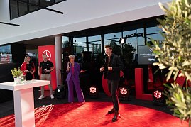 Ein Laufsteg-Moment: Ein junger Mann l&auml;uft &uuml;ber den roten Teppich, w&auml;hrend Moderatorin Mandy Kossira im lila Hosenanzug mit Mikrofon spricht.