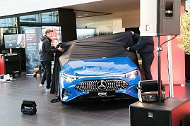 Ein blauer Mercedes CLA wird auf der B&uuml;hne pr&auml;sentiert. Zwei M&auml;nner ziehen ein schwarzes Tuch von der Motorhaube.