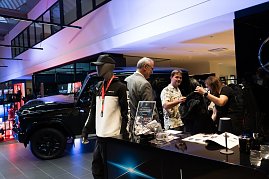Ein Stand mit Mercedes-AMG-Merchandise: Vorne eine Schaufensterpuppe im Trainingsanzug, daneben Besucher, die Kleidung ansehen. Im Hintergrund ein schwarzer Mercedes-Gel&auml;ndewagen.
