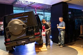 Ein schwarzer Mercedes-Gel&auml;ndewagen steht schr&auml;g auf einer Holzrampe, um seine Gel&auml;ndef&auml;higkeit zu demonstrieren. Zwei M&auml;nner betrachten das Auto aus n&auml;chster N&auml;he.