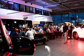 Abendstimmung im Showroom: Viele G&auml;ste sitzen an langen Tafeln, w&auml;hrend im Hintergrund Fahrzeuge und Mercedes-Displays beleuchtet sind.