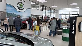 Besucherinnen und Besucher im Autohaus Autowelt Peter während der Jubiläumsfeier zu 130 Jahren koda. Im Ausstellungsraum stehen Fahrzeuge, Kranzdekorationen und ein Tisch mit Sektgläsern.