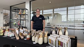 Stand mit regionalen Produkten im Autohaus Autowelt Peter. Eine Frau präsentiert dekorative Gläser mit Gewürz- und Backmischungen, Flaschen und Geschenksets, die auf einem Tisch ausgestellt sind.