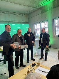 Andreas und Helmut Peter halten Pakete in den Händen und lächeln, daneben stehen 2 Herren von der Dekra