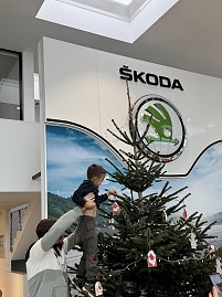 Ein Erzieher hebt das Kind hoch, damit es weiter oben am Baum seinen Anhänger platzieren kann.