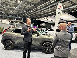 Andreas Peter erklärt einen grauen SUV am Messestand, zwei Zuhörer stehen davor. Im Hintergrund Suzuki-Banner und weitere Autos.