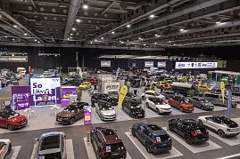 Panoramablick über eine Messehalle mit vielen ausgestellten Autos, Markenständen und großen Werbebannern.