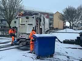 M&uuml;llabfuhr leert eine blaue M&uuml;lltonne auf einer verschneiten Wohnstra&szlig;e.