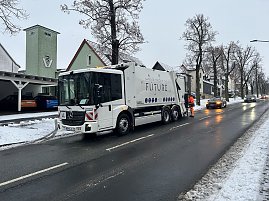 Modernes M&uuml;llfahrzeug Garbage Truck of the Future f&auml;hrt auf winterlicher Stra&szlig;e durch eine Ortschaft.