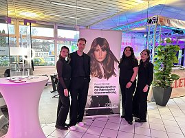 Vier Personen vor L�Or&eacute;al-Stand mit Werbebanner und Eventbeleuchtung.