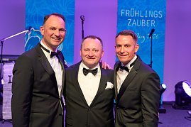 Drei Herren im Smoking stehen beieinander vor der B&uuml;hne und schauen l&auml;chelnd in die Kamera.
