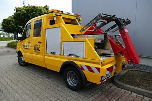 Gelbes ADAC-Servicefahrzeug des Autohaus Peter mit Abschleppvorrichtung, Seitenfächern und rotem Hebearm, geparkt auf einem gepflasterten Hof vor einer grauen Gebäudewand.