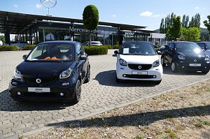 Reihe von Smart-Autos (schwarz und weiß) auf dem Parkplatz vor einem Mercedes-Benz Autohaus mit Peter-Logo in Northeim, im Hintergrund moderner Glasbau, gepflegte Büsche und Bäume unter blauem Himmel.