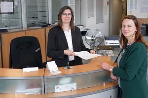 Zwei Frauen am Empfangstresen des Mercedes-Autohauses in Zerbst. Die Mitarbeiterin übergibt ein Dokument an die Kundin, beide lächeln in die Kamera.
