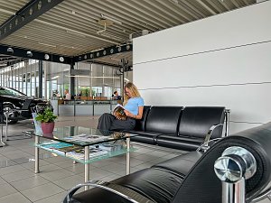Kundenwartebereich im Mercedes-Benz Autohaus Bernburg, eine junge Frau sitzt auf einer schwarzen Ledersitzgruppe und liest eine Brosch&uuml;re, davor ein Glastisch mit Zeitschriften.