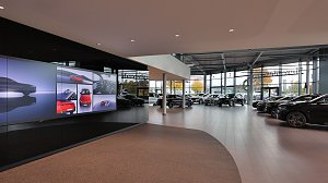 Moderner Ausstellungsraum eines Mercedes-Benz Autohauses mit großem LED-Bildschirm, vielen Neuwagen in heller, verglaster Halle.