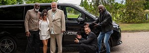 Gruppenfoto vor Shuttlebus: F&uuml;nf Personen, darunter vier M&auml;nner und eine Frau, posieren lachend vor einem schwarzen Mercedes-Benz Shuttlebus mit dem Logo Autohaus Peter.