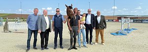 Pressekonferenz auf dem Reitplatz in Immenrode: Sieben erwachsene Personen stehen nebeneinander, darunter ein Reiter mit Pferd und eine Person mit Kind auf dem Arm. Im Hintergrund sind Hindernisse und die Reitplatzanlage zu sehen. Die Veranstaltung dient der offiziellen Vorstellung des Reitturniers Immenrode 2025.