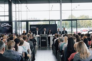 Blick auf das Podium mit der Gesch&auml;ftsf&uuml;hrung und Ausbildungsleitung der Autohaus-Peter-Gruppe. Dahinter gro&szlig;e Fensterfront, davor sitzen die neuen Auszubildenden und G&auml;ste.
