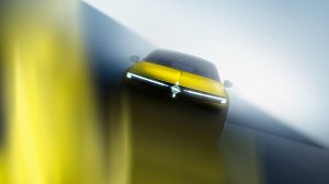 Ein gelbes Auto ist frontal und leicht von unten fotografiert. Das Fahrzeug steht in einer nebeligen, lichtdurchfluteten Umgebung. Die dominante Frontleiste mit schmalen LED-Scheinwerfern bildet eine horizontale Lichtlinie. In der Mitte befindet sich ein kreisf&ouml;rmiges Markenemblem. Die Aufnahme wirkt dynamisch und futuristisch durch starke Unsch&auml;rfen und Lichtreflexe.