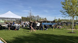 Ein Schild "Kreativwiese", dahinter Pavillons und mehrere Frauen an Biertischgarnituren.