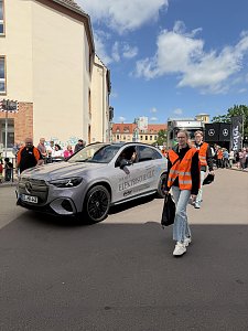 Man sieht einen grauen GLC und dahinter den grauen eActros. Neben dem GLC laufen 4 Radengel.