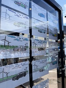Man sieht viele Bilder, die von Kindern mit bunten Stiften ausgemalt worden sind. Die Bilder kleben an der Glasscheibe des Eventstands.