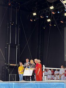 Sven Schulze (MP des Landes Sachsen-Anhalt) und Dr. Silvia Ristow (OB Bernburg (Saale)) mit zwei weiteren Personen und einer Moderatorin auf der B&uuml;hne w&auml;hrend einer Scheck&uuml;bergabe.