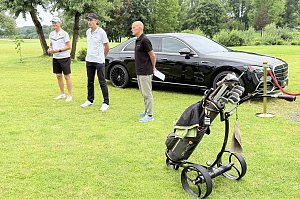 Turnierleitung begr&uuml;&szlig;t die Teilnehmenden auf dem Golfplatz vor einer schwarzen Mercedes-Benz Limousine.