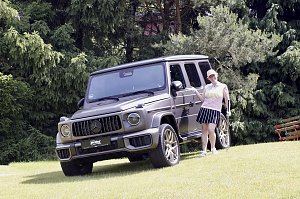 Teilnehmerin posiert l&auml;chelnd neben einer ausgestellten Mercedes G-Klasse auf dem Golfplatz.
