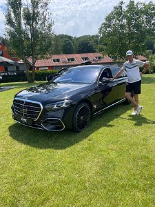 Golfspieler lehnt an einer schwarzen Mercedes-Benz Luxuslimousine auf dem Veranstaltungsgel&auml;nde.