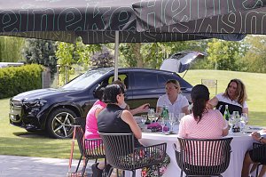 G&auml;ste sitzen unter Sonnenschirmen zusammen und genie&szlig;en Gespr&auml;che auf der Terrasse neben einem Mercedes SUV.