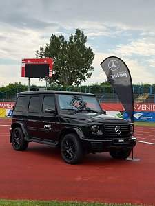 Eine schwarze Mercedes-Benz G-Klasse des Autohauses Peter, ausgestellt direkt auf der roten Laufbahn im Stadion neben einer Werbefahne.