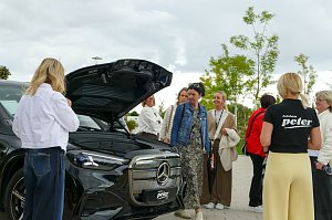 Eine Gruppe von Frauen, die sich im Freien um einen schwarzen Mercedes-Benz GLC mit ge&ouml;ffnetem Frunk versammelt haben und das Fahrzeug betrachten.