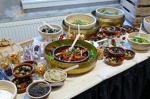 Ein reichhaltiges Buffet, das mit verschiedenen kleinen Vorspeisen, Salaten, eingelegtem Gem&uuml;se und Dip-Schalen samt kleinen Beschriftungstafeln angerichtet ist.
