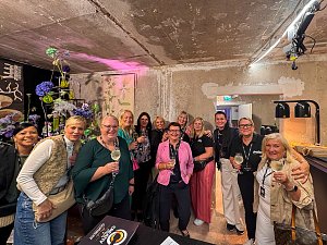 Eine Gruppe von Frauen, die mit Getr&auml;nken in den H&auml;nden in einem rustikalen Innenraum f&uuml;r ein gemeinsames Foto posieren.