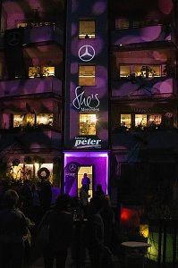 Eine Fassade, die lila beleuchtet ist und Logos von Mercedes, She�s Mercedes sowie der Autohaus Peter Gruppe tr&auml;gt.
