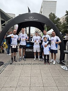 Man sieht das Autohaus Peter Firmenlauf-Team vor dem Lauf, vor dem schwarzen Pavillon. Alle haben die gleichen wei&szlig;en Sport-Shirts an, lachen in die Kamera, manche machen den Daumen hoch.