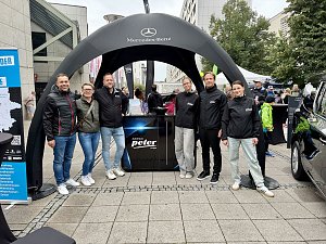 Man sieht das Team vom Autohaus Peter vor einem schwarzen, aufblasbaren Pavillon mit Mercedes-Benz Aufdruck. In der Mitte steht ein schwarzer Counter, mit Logo-Aufdruck der Autohaus Peter Gruppe in Wei&szlig;.