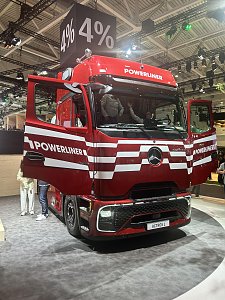 Dunkelroter Mercedes-Benz Lkw von vorne links auf einer Messe. Die T&uuml;ren stehen offen. Auf der Front sind wei&szlig;e Querstreifen und der Schriftzug POWERLINER zu sehen. &Uuml;ber dem Lkw h&auml;ngt ein schwarzer W&uuml;rfel mit der wei&szlig;en Aufschrift 4%.