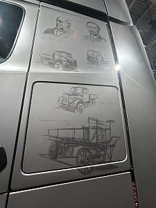 Silberne Lkw-Seitenwand mit feinen Zeichnungen. Oben sind Portr&auml;ts von Carl Benz und Gottlieb Daimler. Darunter sind verschiedene historische Lastwagen skizziert, vom h&ouml;lzernen Ur-Modell bis zum moderneren Hauben-Lkw.