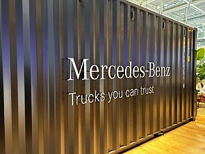 Dunkelgraue Containerwand aus Wellblech auf einer Messe. In der Mitte prallt der silberne, erhabene Schriftzug Mercedes-Benz hervor. Darunter steht der wei&szlig;e Slogan Trucks you can trust.