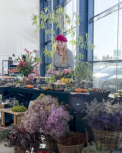 Floristin hinter einem herbstlich dekorierten Stand mit Blumenstr&auml;u&szlig;en, Gestecken, K&uuml;rbissen und Trockenblumen.


