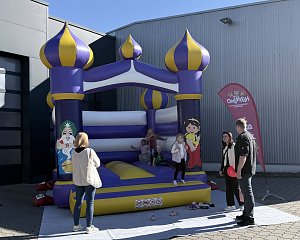 Kinder spielen bei sonnigem Wetter auf einer gro&szlig;en lila-gelben H&uuml;pfburg auf dem Au&szlig;engel&auml;nde der Autowelt Peter.